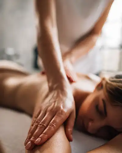 A woman lying on a massage table is receiving a massage from another woman
